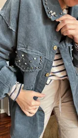 Camisa de pana azul con cuello clásico, cierre frontal con botones dorados, bolsillos con solapa y detalles de strass en cuello y bolsillos. Mangas largas con puños abotonados.