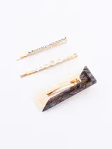 Set de tres pinzas para el pelo doradas, con diferentes diseños: una con strass, otra con perlas y otra con diseño geométrico en blanco y negro.