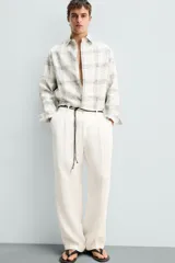 Pantalón color crema de lino, corte relaxed fit, con pliegues frontales, bolsillos laterales y traseros de vivo.