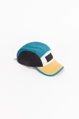 Gorro de visera de cinco paneles con diseño color block en azul, amarillo y negro. Presenta un parche con logo en el panel frontal.