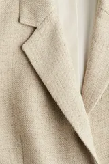 Blazer color beige de corte holgado con solapas de muesca, hombreras, abertura y botón en los puños, bolsillos delanteros ribeteados y bolsillo superior ribeteado. Forrado.