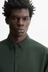 Camisa de vestir verde oscuro, corte slim fit, con cuello italiano, mangas largas con puños abotonados y cierre frontal con botones.