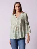 Blusa de gasa estampada color salmón con flores blancas, marca Ruby Rd. Cuello a la base, escote en V y abertura central con botones. Delantera con plisados. Largo de manga ¾ con terminación amplia.