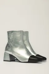 Botas cortas plateadas de cuero con puntera negra, taco cuadrado y cierre lateral.