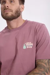 Remera de algodón color verde salvia, con cuello redondo y manga corta. Presenta un pequeño parche estampado en el pecho con un diseño gráfico.