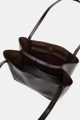 Bolso de hombro tipo shopper de cuero sintético color marrón oscuro, con pespuntes decorativos en el cuerpo y asas delgadas. Cierre principal con botón imantado y bolsillo interior con cremallera.