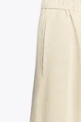 Pantalón ancho color verde oliva confeccionado en lino. Tiro alto con cintura elástica ajustable con cordón y pinzas delanteras. Presenta bolsillos laterales y traseros. Incluye cinturón de la misma tela con apliques metálicos.