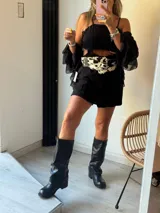 Bota de caña media-alta de cuero negro, estilo biker o motoquera, con caña arrugada y hebilla ajustable en el tobillo. Posee un taco bajo y suela gruesa.