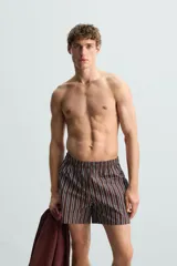Bañador corto de hombre con estampado de rayas verticales en marrón, blanco y azul. Cuenta con cintura elástica ajustable con cordón, bolsillos laterales y trasero.