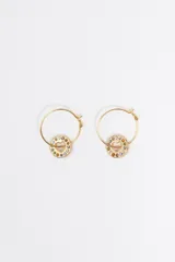 Pendientes de aro dorados con un dije circular que presenta un calado en forma de corazón en el centro, rodeado por pequeños cristales de diversos colores. Cuentan con un cierre de gancho metálico.