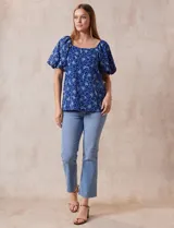 Blusa azul con estampado floral blanco, cuello cuadrado, mangas cortas abullonadas y frunce en los hombros.