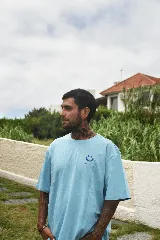 Remera celeste de algodón con cuello redondo y mangas cortas. Estampado pequeño en el frente con el logo de la marca y un vaso con una carita sonriente.