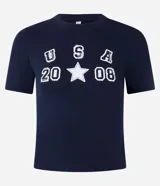Remera baby look azul marino con estampado frontal de letras "USA" apiladas verticalmente sobre el número "20" y el número "08" separados por una estrella blanca.
