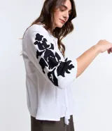 Blusa amplia de viscolino color blanco con bordados florales negros en mangas y escote, lazo en el cuello y mangas 3/4 con puño ajustado.
