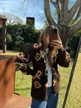 Saco marrón de lana tejido a mano con botones y estampado de flores en tonos naranja, blanco y verde.