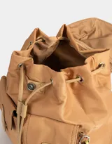 Mochila de tela color lila, con solapa con broche y tira de ajuste, doble bolsillo frontal con broche y pouch con charm lateral en forma de cartera.