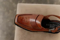 Zueco negro con textura croco, diseño tipo mocasín y tira regulable al talón.