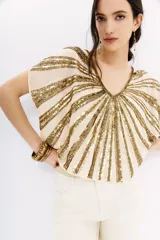 Blusa color crema con escote en V y mangas cortas tipo kimono. Presenta un diseño de rayas horizontales con lentejuelas doradas.