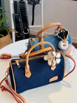 Cartera tipo bowling de jeans azul con detalles en cuero sintético color camel. Incluye llavero de peluche y dije de flor.
