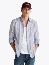 Camisa de mangas largas a rayas verticales azules y blancas, confeccionada en popelín de puro algodón con tecnología Flex que le confiere elasticidad. Tiene cuello abotonado, puños redondeados con botón y logo de Tommy Hilfiger bordado en el pecho.