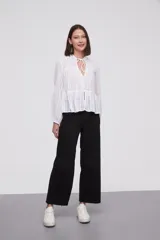 Blusa blanca con rayas verticales, cuello con lazo, mangas largas y corte holgado.