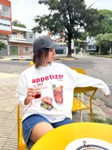 Buzo blanco de corte oversize con estampado de un trago y la frase "appetizer o'clock my only recipe w/ friends".