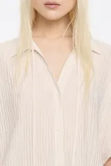 Camisa color beige estilo capa confeccionada en viscosa con textura. Cuenta con cuello camisero con lazo, manga corta murciélago y cierre frontal con botones.