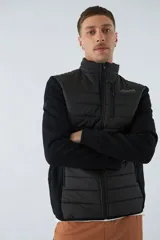 Campera negra con cuerpo acolchado de nylon y mangas de felpa. Tiene cuello alto, cierre frontal, bolsillos laterales con cierre, logo estampado en el pecho y logo de goma en la manga.