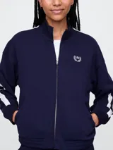 Campera deportiva Gap azul marino con cierre frontal, cuello alto y logo bordado en el pecho. Presenta dos líneas blancas verticales a lo largo de las mangas.