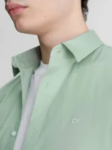 Camisa verde claro de popelín elástico, corte slim, con cierre frontal de botones, mangas largas y logo de Calvin Klein bordado en el pecho.