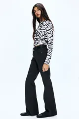 Jean de cinco bolsillos color negro, con tiro bajo y cierre de botón. Presenta un corte ajustado en la parte superior y piernas acampanadas.