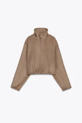 Cazadora corta color marrón claro, de cuello alto y manga larga. Tiene bolsillos laterales y cierre frontal con cremallera metálica.