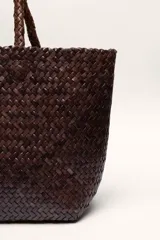Bolso tipo tote de cuero vacuno, completamente trenzado a mano. El color es marrón oscuro, casi chocolate. Posee dos asas de hombro trenzadas.