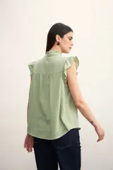 Camisa color amarillo pálido con cuello mao, sin mangas, con volados en los hombros y en el frente.