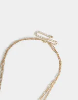 Collar corto dorado de doble cadena con dijes de cerámica, perlas, corazón y moño.