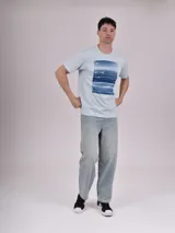 Remera celeste de manga corta con estampa rectangular con imagen del mar y texto en la parte superior.