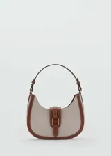 Bolso tipo hobo de lona color beige con detalles en cuero marrón. Tiene asa corta ajustable, cierre con solapa y botón magnético, bolsillo interior y forro de algodón.