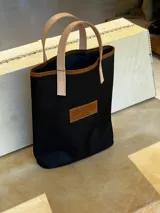 Bolso matero negro de lona con detalles en cuero color suela, doble asa corta de cuero y etiqueta de cuero con logo de la marca.