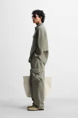 Sobrecamisa verde militar de lino, corte relaxed fit, con cuello solapa, manga larga con puños abotonados, bolsillos de parche con solapa en el pecho, aberturas laterales en el bajo y cierre frontal abotonado.