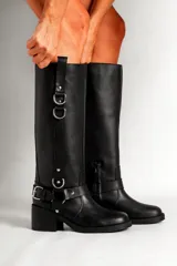 Bota de cuero negra de caña alta con hebillas y apliques metálicos.