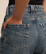 Pantalón mom confeccionado en jeans celeste, con cintura con trabillas dobles, cierre por botón y cremallera, bolsillos delanteros y traseros, y lateral desplazada.