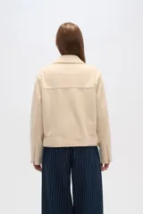 Chaqueta negra con cuello solapa, cierre cruzado con cremallera, cinturón con hebilla, bolsillos laterales con cremallera y detalles de botones metálicos.