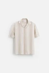 Camisa de manga corta con cuello bowling y corte relaxed fit. Diseño a rayas verticales en tonos beige y blanco. Cierre frontal con botones y bajo con aberturas laterales.