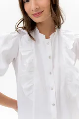 Blusa de lino color rojo con volados frontales que enmarcan el pecho, cuello redondo con mini volado y mangas 3/4 abullonadas con puño elástico. Presenta un cierre frontal con botones y una silueta relajada.