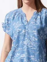 Blusa celeste estampada con motivos de playa, con cuello a la base y escote en V. Mangas cortas con detalle fruncido.
