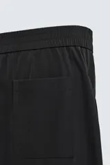 Pantalón negro de corte amplio confeccionado en tejido técnico, con cintura elástica, bolsillos delanteros y trasero de parche. Presenta bandas laterales a tono.