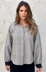 Camisa beige a rayas verticales finas, con cuello clásico, mangas largas abullonadas con puños marrones y cierre frontal con botones.