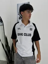 Chomba de manga corta con cuello polo y tapeta de dos botones. Diseño bicolor blanco y negro, con paneles negros en mangas y laterales. Presenta estampados en negro: logo de 'Bangkok Club' y texto 'BNK CLUB' en el frente, y el número '00' en el pecho derecho.