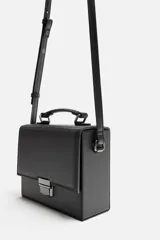 Bandolera rígida negra en formato caja con cierre metálico y asa de hombro ajustable.