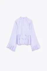 Camisa lila de cuello redondo y manga larga con volantes en el mismo tejido. Cierre en la espalda con aberturas y botones.